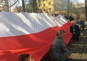 Słuchacze i pracownicy szkoły unoszą kilkumetrową flagę Polski z okazji Święta Niepodległości